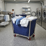 Chariot à linge bleu utilisé dans une blanchisserie professionnelle. Il est rempli de linge, notamment de serviettes, draps et o