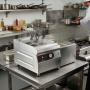Cuiseur à pâtes professionnel en acier inoxydable installé sur un plan de travail dans une cuisine de restaurant. De la vapeur s