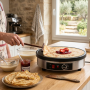 Crêpière électrique professionnelle installée sur un plan de travail en bois dans une cuisine lumineuse. Une personne soulève un