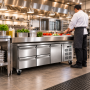 Soubassement réfrigéré en inox installé dans une cuisine professionnelle, sous un plan de préparation. Un cuisinier découpe des 