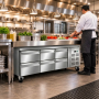 Table réfrigérée inox à six tiroirs installée dans une cuisine professionnelle moderne. Un cuisinier en tenue blanche prépare de