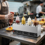 Chauffe-sauces professionnel à quatre bouteilles installé sur un plan de travail en inox dans une cuisine de restauration rapide