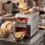 Grille-pain convoyeur professionnel en inox installé sur un buffet de petit-déjeuner, entouré de pains, viennoiseries et confitu