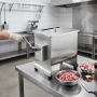 Mélangeur à viande professionnel en inox installé sur une table de travail dans une cuisine professionnelle. Une personne portan
