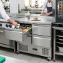 Table réfrigérée professionnelle inox à quatre tiroirs intégrée dans une cuisine de restaurant. Un cuisinier ouvre un tiroir con